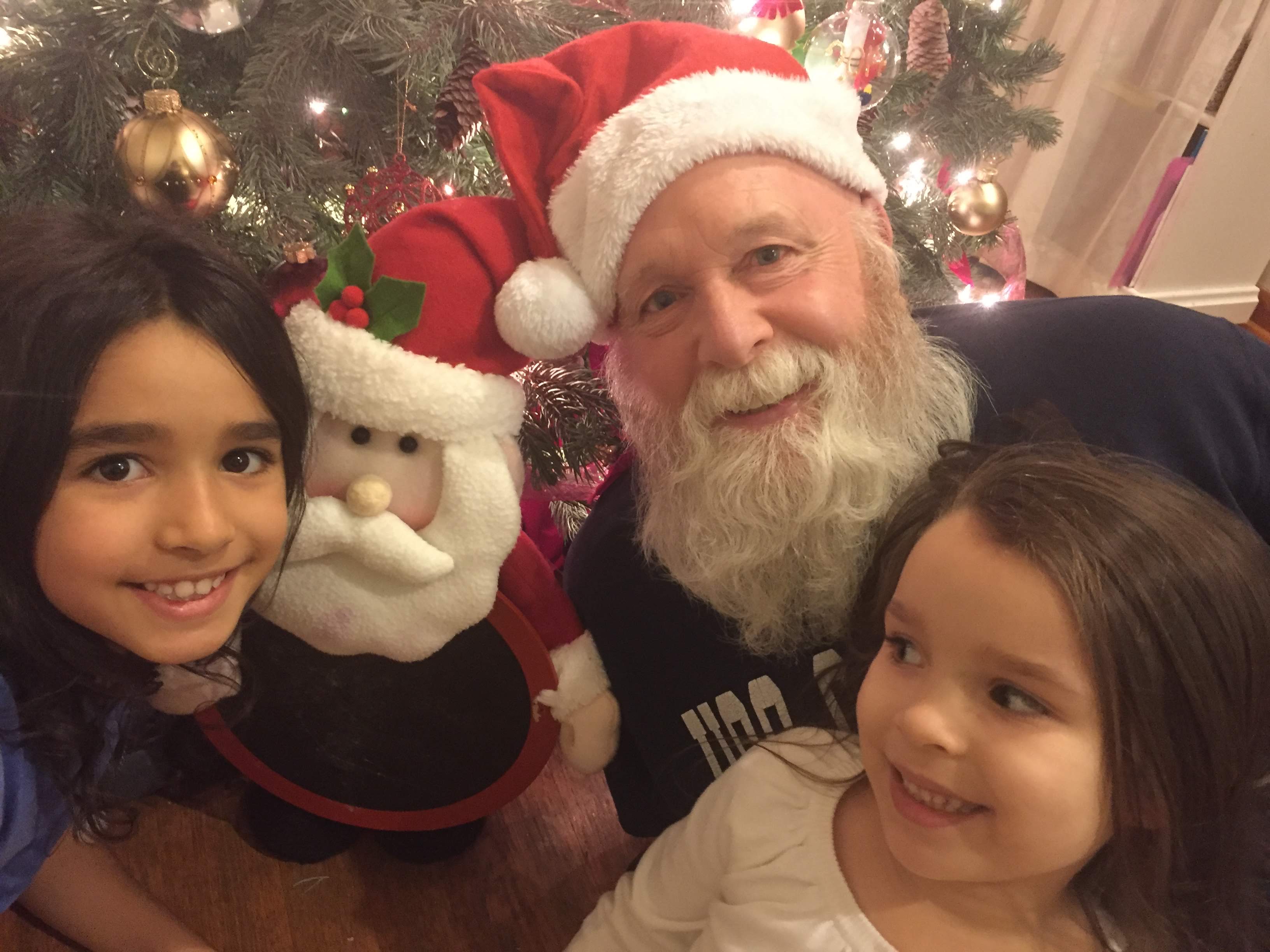 Tom as Santa with two girls by the Christmas tree